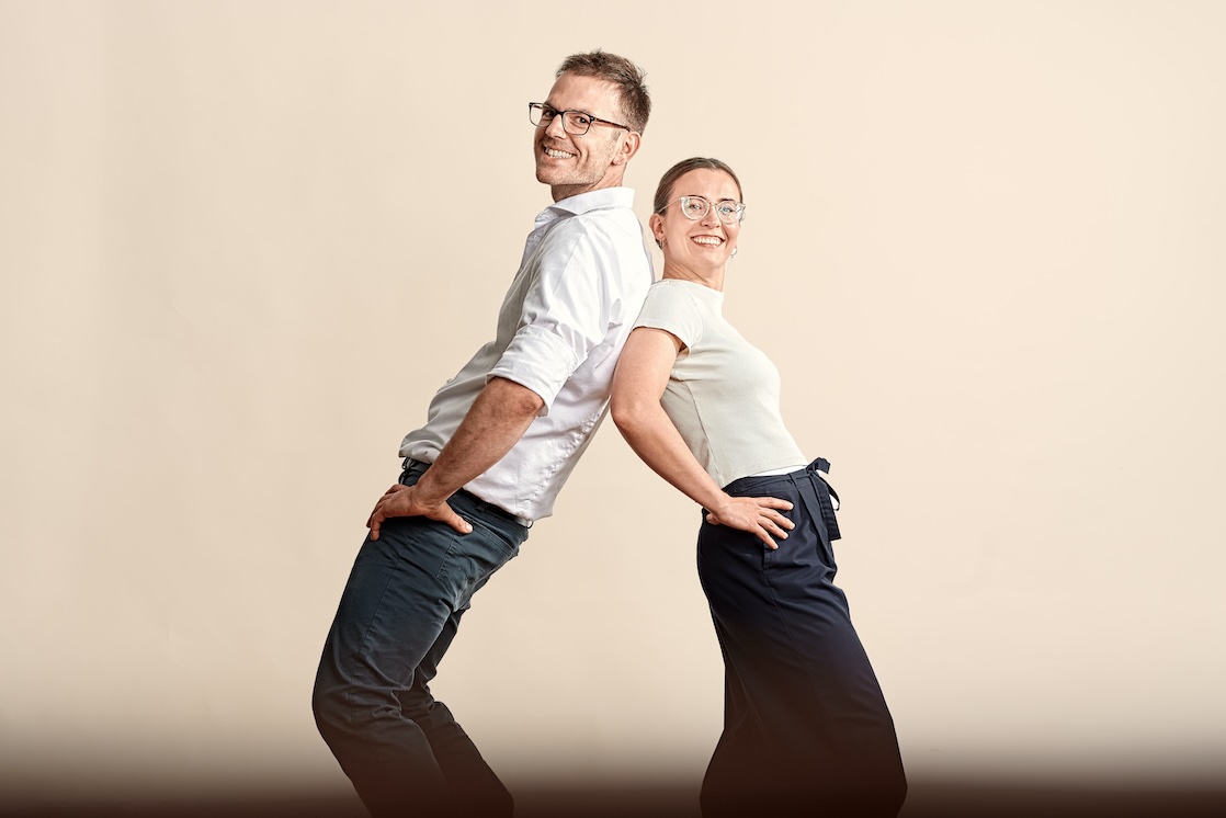 Die Osteopathen Alina Serafin und Utz Kieltsch stehen Rücken an Rücken und lächeln. Diese Darstellung zeigt das Team von Osteopathie und Pilates in Wiesbaden.